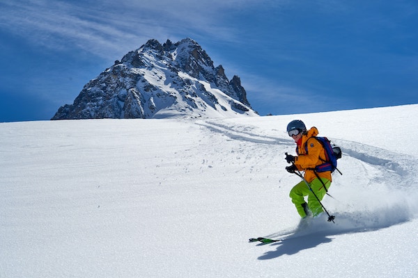 A man skiing in the mountains on a white snow during cold and sunny day with a high mountain in the background