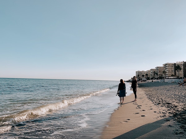 Two women walking on the sand at Malagueta Beach in Malaga
