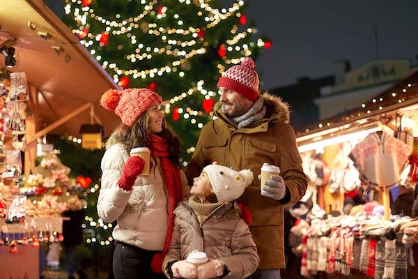 family, winter holidays and celebration concept - happy mother, father and little daughter with takeaway drinks at christmas market on town hall square in tallinn, estonia