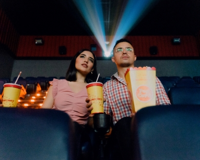 A couple watching a movie while holding popcorn and drinks during a film festival.