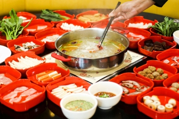 A bowl of family hotpot soup simmering on a steel pot with small red bowls of ingredients all around.
