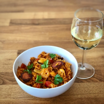 A bowl of paella and a glass of white wine.
