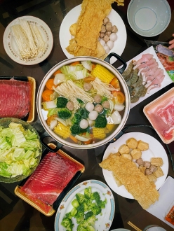 A simmering pot of soup and several plates of raw meat and vegetables.