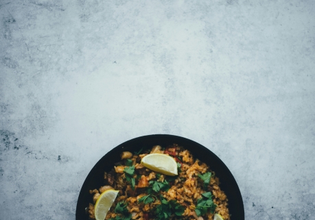 A pan of paella with leafy vegetables and green peas.