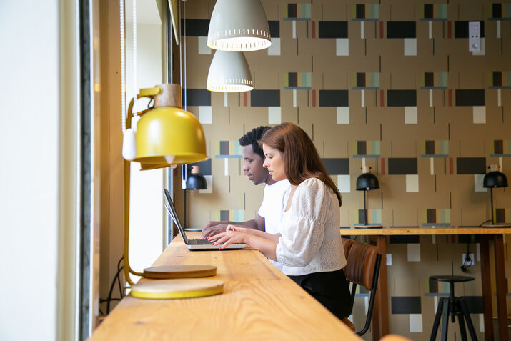Concentrated professionals sit together, working on laptops in a coworking space.
