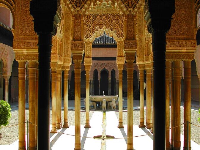 Ornate columns of the Palace of the Alhambra in Granada, Spain, framing a view of the Court of the Lions.