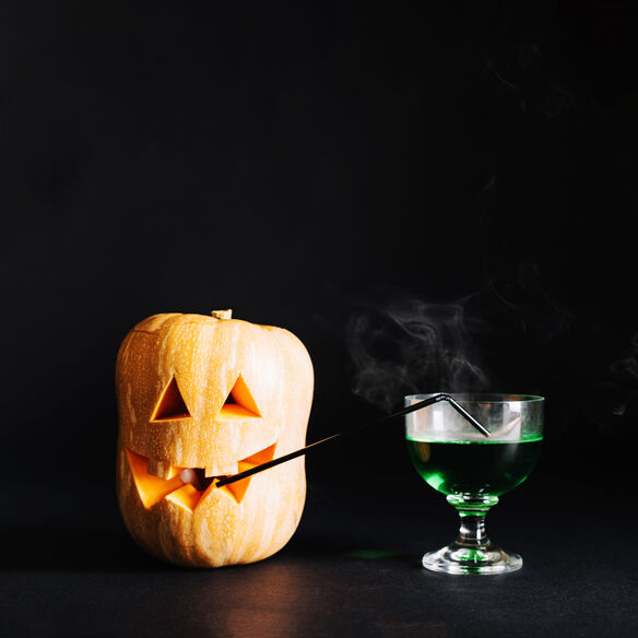 A vibrant arrangement of a carved pumpkin next to a glass of green drink, set against a dark background.