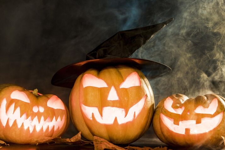 Three carved pumpkins with spooky faces surrounded by swirling smoke, embodying the Halloween spirit.